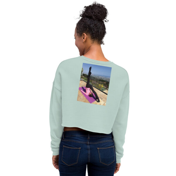 Back of woman modelling a seafoam colored cropped sweatshirt with a graphic of a woman in a pilates pose.