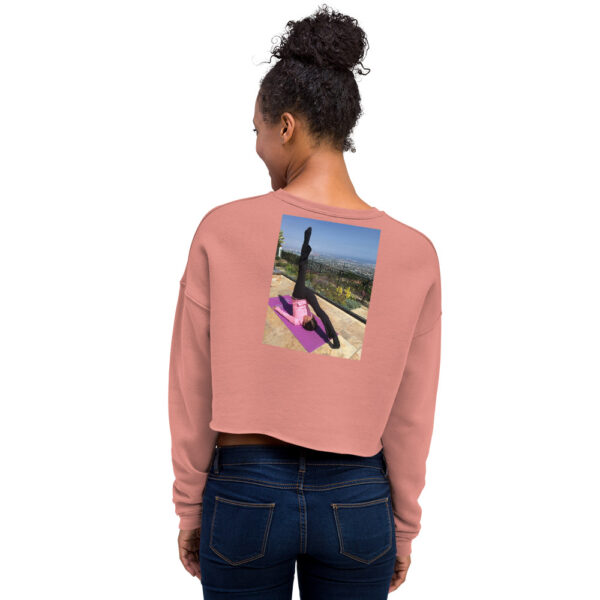 Back of woman modelling a muted pink colored cropped sweatshirt with a graphic of a woman in a pilates pose.